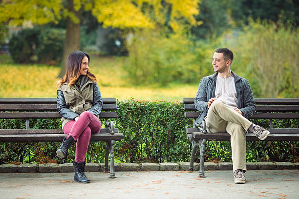 People in a Park Two young people sitting on benches in a park and talking face to face stock pictures, royalty-free photos & images