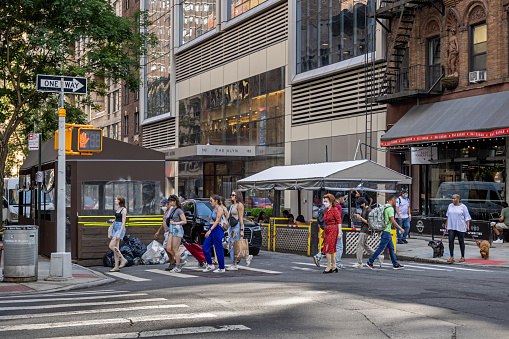 Manhattan, New York, NY, USA - June 30, 2022: Pedestrians in a zebra crossing in front of outdoor restaurants at Lexington Avenue close to East 87th Street