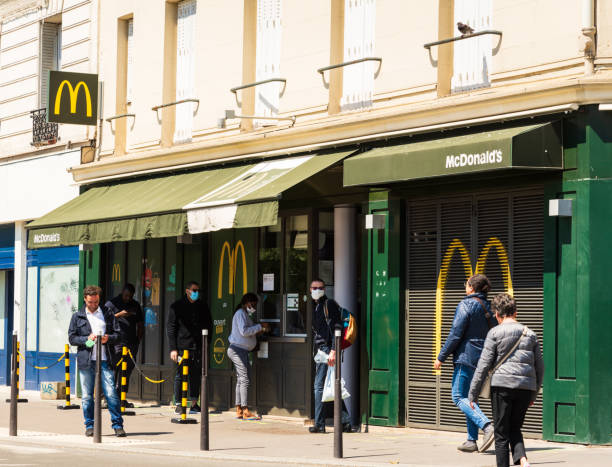 People in masks keep social distance waiting to buy food at McDonald in Parisian suburb. Coronavirus lockdown end, start of deconfinement (easing restrictions). stock photo