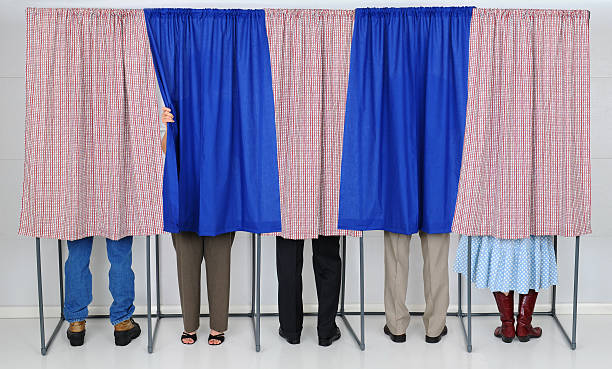People in Voting Booths A row of five voting booths with men and women casting their ballots at a polling place. Horizontal format, only showing the legs of the voters, people are unrecognizable.. voting booth stock pictures, royalty-free photos & images