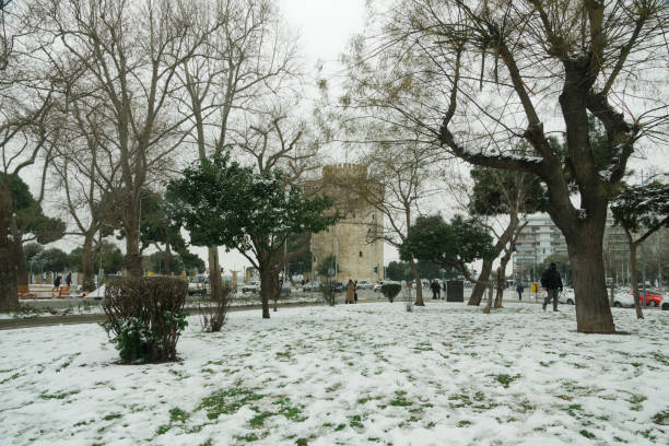 People in warm clothes and covid-19 masks around White Tower landmark with snow falling. stock photo