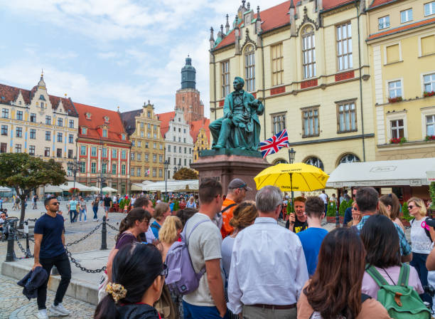 People on a free guided tour listening in front of the Aleksander Fredro Monument at central market square in Wroclaw Wroclaw, Poland - August 16, 2019: Tourists on a free guided tour listening to the english speaking tour guide in front of the Aleksander Fredro Monument at Central Market Square wroclaw photos stock pictures, royalty-free photos & images