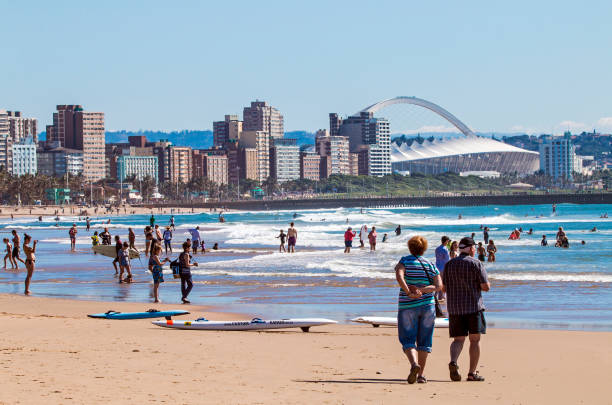 People on Visit to Beach Against Durban City Skyline DURBAN, SOUTH AFRICA ; APRIL 24, 2017: Many unknown people on morning visit to beach against Durban city skyline and Moses Mabhida Stadium  in South Africa durban stock pictures, royalty-free photos & images