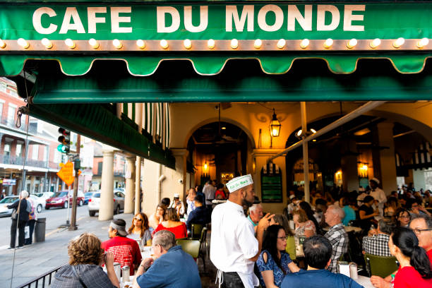 People ordering food in Cafe Du Monde restaurant, eating beignet powdered sugar donuts, drinking chicory coffee, waiter taking order stock photo