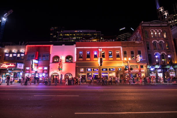 People walk along Broadway in Nashville Tennessee USA at night Nashville, Tennessee - June 20, 2019:  People walk along the businesses and bars on Broadway in Nashville Tennessee USA.  Broadway is known for its honky-tonks, Music and record stores. broadway nashville stock pictures, royalty-free photos & images