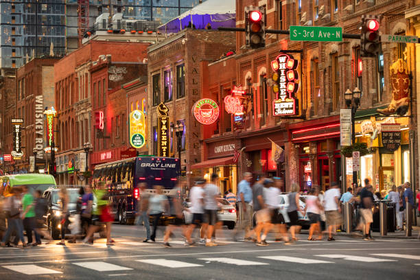 People walk along Broadway in Nashville Tennessee USA Nashville, Tennessee - June 20, 2019:  People walk along the businesses and bars on Broadway in Nashville Tennessee USA.  Broadway is known for its honky-tonks, Music and record stores. broadway nashville stock pictures, royalty-free photos & images