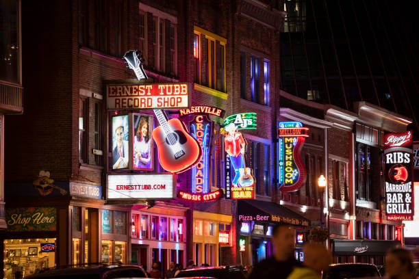People walk along Broadway in Nashville Tennessee USA Nashville, Tennessee - June 20, 2019:  People walk along the businesses and bars on Broadway in Nashville Tennessee USA.  Broadway is known for its honky-tonks, Music and record stores. broadway nashville stock pictures, royalty-free photos & images