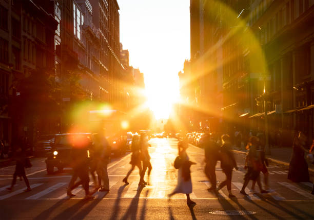 People walking across the street in New York City with bright light of sunset stock photo