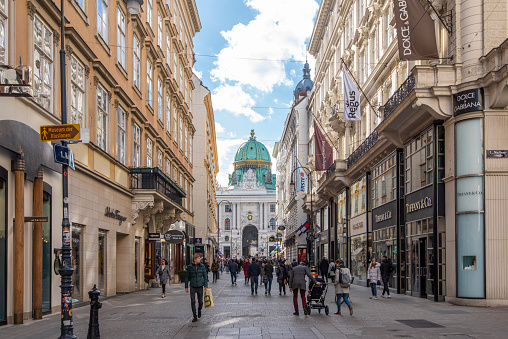 People walking in a pedestrian street at downtown Vienna, Austria. In the background the Ofburg Imperial Palace facade and dome.