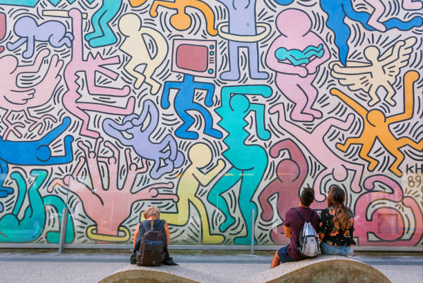 People watching on wall with artwork by modern artist Keith Haring, famous in pop-art style stock photo