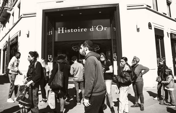People wearing protective masks walk at Rivoli street;  waiting in line (keeping social distance) to enter Histoire d'Or jewelry store. Coronavirus lockdown end. stock photo