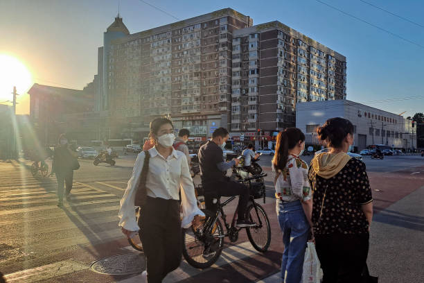 People with face masks waiting for green light to cross road during coronavirus pandemic at sunset in Beijing. stock photo