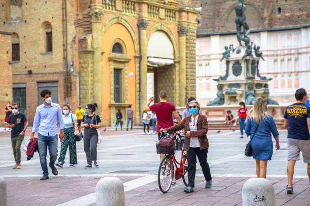 people with surgical mask in Bologna Italy Bologna, Italy - May 9, 2020: bikes and people with surgical mask in Piazza Maggiore central square with Neptune statue fountain and San Petronio basilica. Covid-19 day after lockdown. neptune roman god stock pictures, royalty-free photos & images