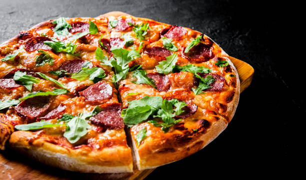 pizza pepperoni con mozzarella, salame, salsa di pomodoro, pepe, spezie e rucola fresca. pizza italiana su sfondo ardesia nera grigio scuro - pizza foto e immagini stock