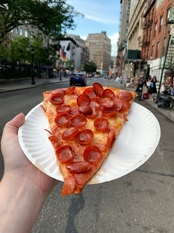 A slice of pepperoni pizza held on a New York City street.