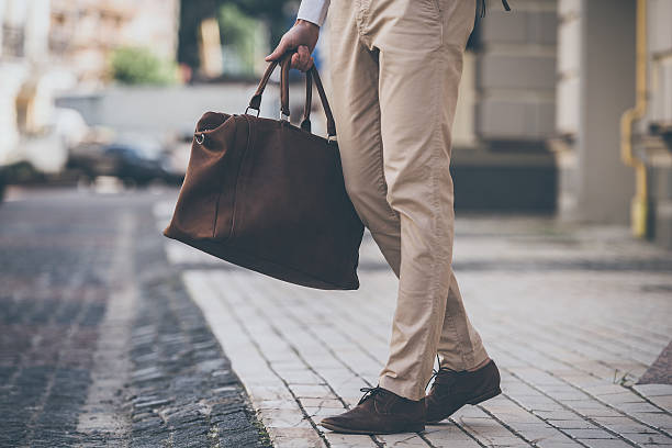 Perfect match. Close-up of man holding leather bag while walking outdoors pants stock pictures, royalty-free photos & images