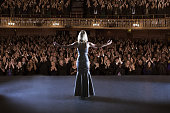istock Performer standing with arms outstretched on stage in theater 476806603