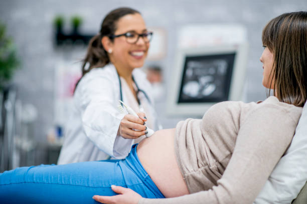 Performing An Ultrasound A pregnant Caucasian woman is indoors in a medical clinic. She is lying down while having an ultrasound. Her doctor is smiling with her while performing the procedure. obstetrician photos stock pictures, royalty-free photos & images