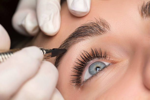 Permanent eyebrow makeup. Cosmetologist applying tattooing of eyebrows. Close up shoot. stock photo