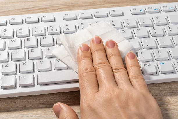 Person hand cleaning the white desktop keyboard with a wet disinfecting wipe. Sanitizing of workplace, surface of desk and keyboard. Routine lifestyle during a covid and flu epidemic. Health care. stock photo
