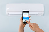 istock Person Hand Holding Mobilephone Near Air Conditioner 1324470422
