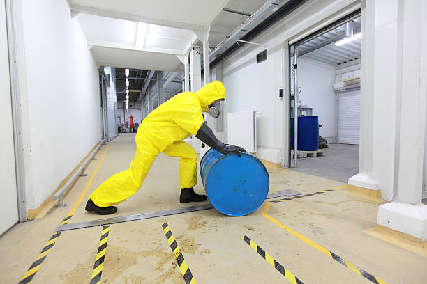 Person in yellow protective gear rolling blue toxic barrel stock photo