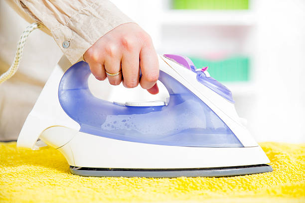 Close-up Of Woman's Hand Ironing Clothes On Ironing Board