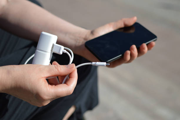 A person is holding a portable power bank charger with smartphone Close up of portable power bank in focus with charging cable and hand holding a smartphone at the back battery charger stock pictures, royalty-free photos & images