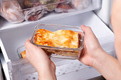 A person is taking a container of frozen casserole or lasagne out of the freezer. Concept of ready made frozen dishes and saving time on cooking food.