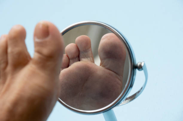 Person looking at the sole of the foot in a mirror. Person looking at the sole of the foot in a mirror, to check if there is no diabetic foot, as possible sores foot exam diabetes stock pictures, royalty-free photos & images