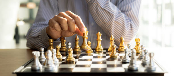 Person playing chess board game, business man concept image holding chess pieces like business competition and risk management, planning business strategies to defeat business competitors. stock photo