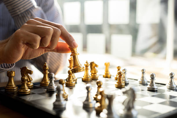 Person playing chess board game, business man concept image holding chess pieces like business competition and risk management, planning business strategies to defeat business competitors. stock photo