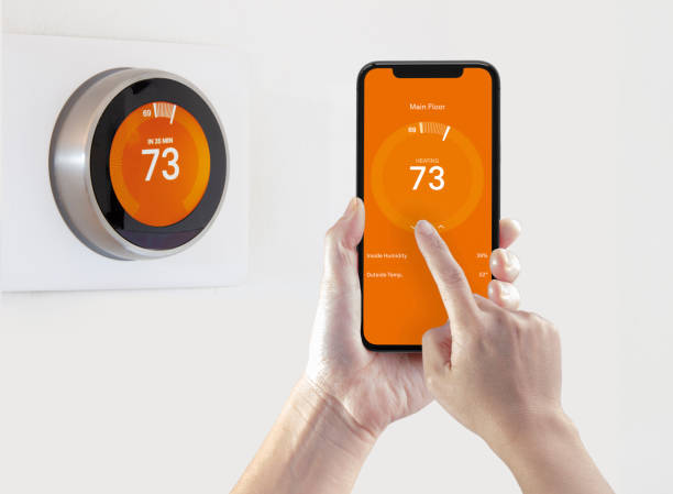 A person using a smart phone application warming up the room temperature with a wireless smart thermostat on a white background. A person using a smart phone application warming up the room temperature with a wireless smart thermostat on a white background. fahrenheit stock pictures, royalty-free photos & images