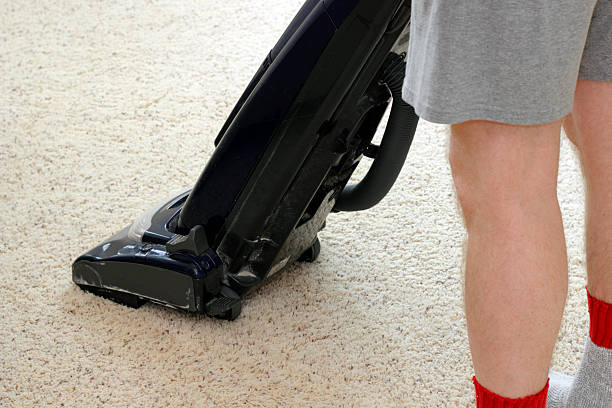 Person Vacuuming Carpet Lower half of a man wearing shorts vacuuming a tan rug with an upright vacuum as part of his housecleaning chores.. good posture stock pictures, royalty-free photos & images