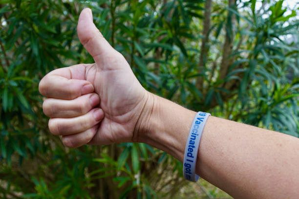 Person wearing a COVID-19 vaccination wristband, giving a thumbs up stock photo