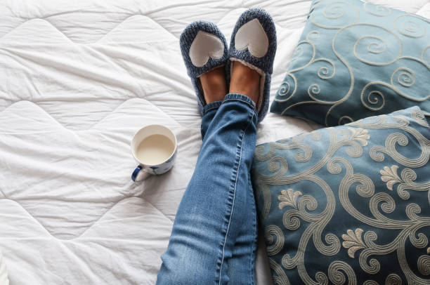 Personal View of Senior Woman Legs Relaxing on Bed with Blue Slippers During Afternoon Tea Break stock photo
