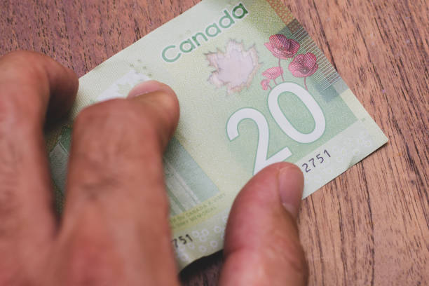 Persons hand giving the Currency of the Canada - One green twenty dollar notes spread out on a brown table background. Money exchange. stock photo