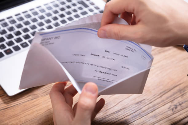 Person's Hand Removing Paycheck From The Envelope Elevated View Of Person's Hand Removing Paycheck From The Envelope Over Wooden Desk wages stock pictures, royalty-free photos & images