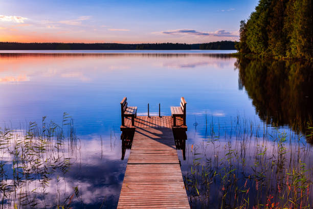 Perspective view of a wooden pier with chairs on the lake at sunset stock photo