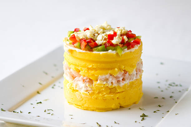 Peruvian Cuisine Dish called Causa made with yellow potatoes and shrimp, topped with red and green peppers and egg.