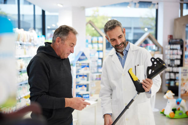 A pharmacist shows a crutch to a senior client. stock photo