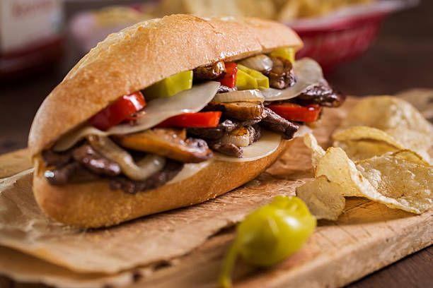 Philly Cheese Steak A philly cheesesteak sandwich with mushrooms, provolone cheese, bell pepper, pepperoncini pepper, and caramelized onion on a bun with chips. roast beef sandwich stock pictures, royalty-free photos & images