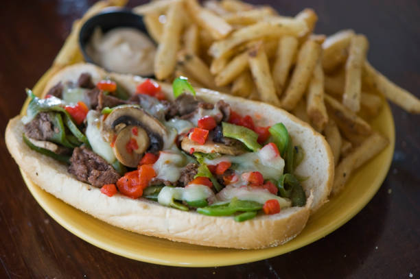 Philly cheese steak sandwich. Sandwich. Classic American sandwich with ham, turkey, crispy Bacon, melted Swiss & cheddar cheese, caramelized onions, lettuce, tomato, on a toasted brioche bun and served with crispy French fries. American Bar food favorite. stock photo