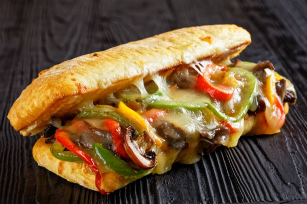 Philly cheese steak sandwich with roasted beef, pepper, caramelized onion, mushrooms and melted cheese on a black wooden table, close-up stock photo