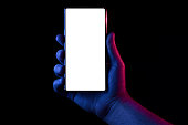 Phone in hand. Silhouette of male hand lit with blue and red neon lights holding bezel-less smartphone on black background. Screen is cut with clipping path.