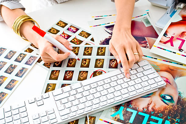 Photo editor at work Focus on hands of women photo editor selecting the best picture for Beauty/Fashion Magazine. She pointing red marker pictures on the printouts and other hand typing on keyboard. editorial photos stock pictures, royalty-free photos & images