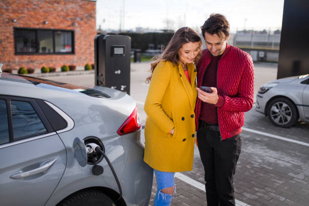 Photo of a young couple on a parking lot, charging their electric car stock photo