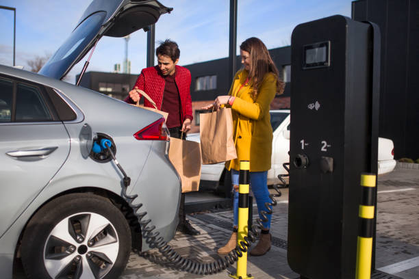 Photo of a young couple on a parking lot, charging their electric car stock photo