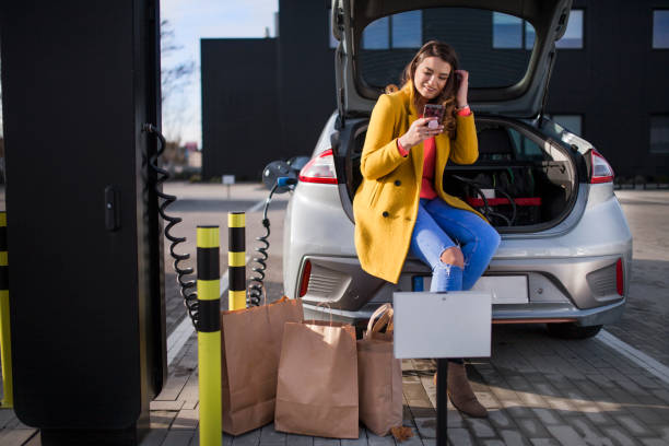 Photo of a young woman on a parking lot, charging her electric car stock photo