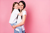 Photo of beautiful young mother hold arms little daughter two ladies, hugging best friends lovely feelings eyes closed wear casual t-shirts jeans isolated pastel pink color background